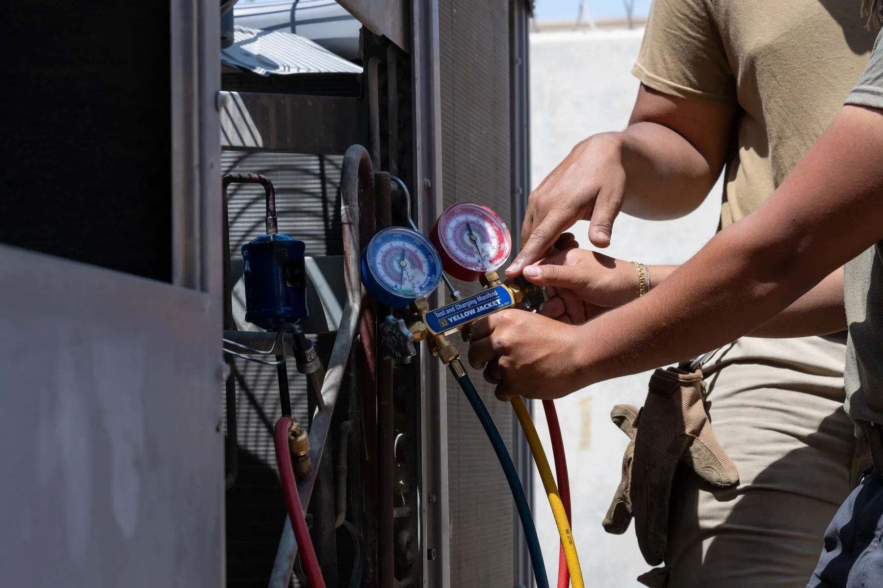 An HVAC technician connects refrigerant gauges to an air-conditioning unit