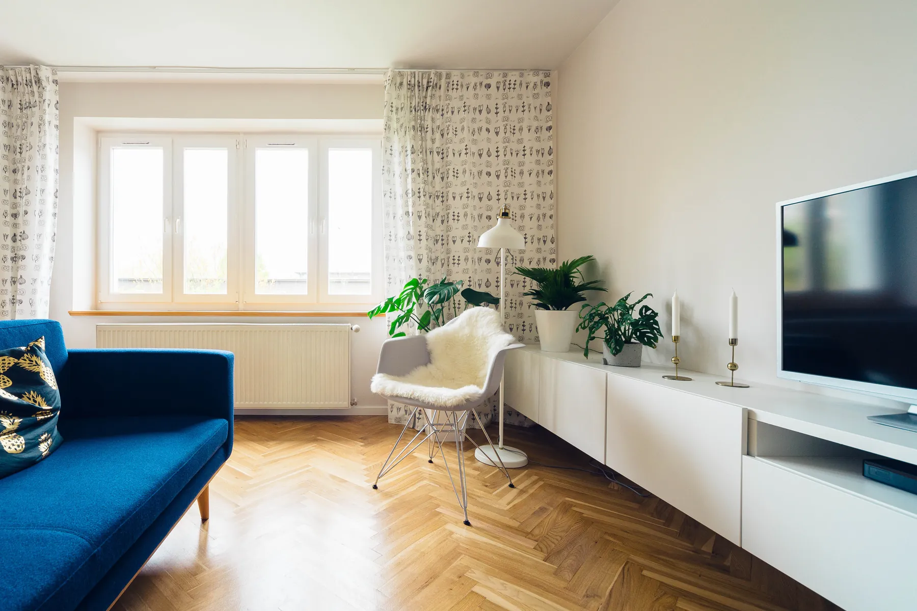 A bright, staged living room with a blue sofa, herringbone floor and tall windows