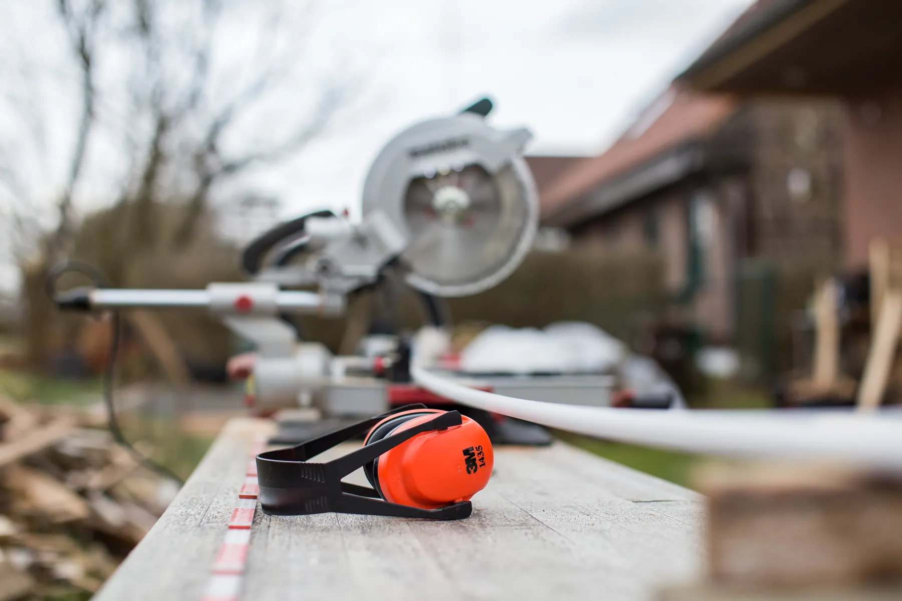 A miter saw and orange ear protectors on a workbench outside a house under renovation